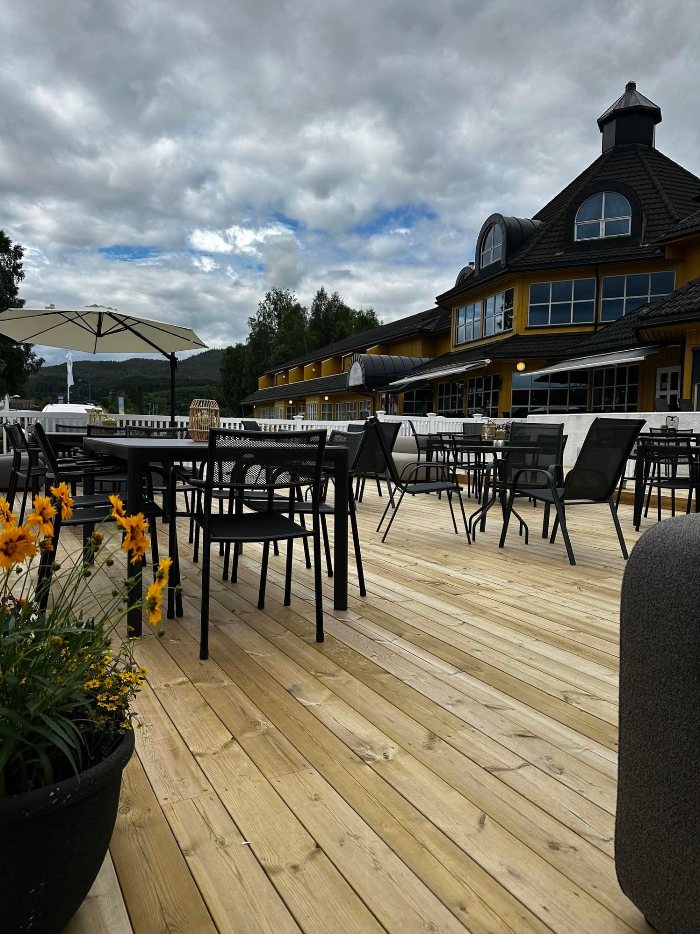 Uteservering og gule bygninger ved Grong Hotell under skydekket himmel